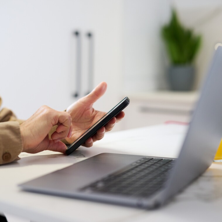 A person using a phone and a computer to exchange currency online through Urbo Internet Bank